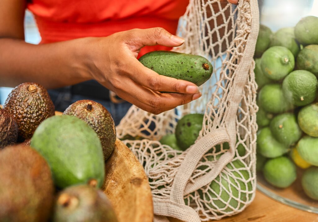 Hands, avocado and bag with a woman customer shopping in a grocery store for a health diet or nutri